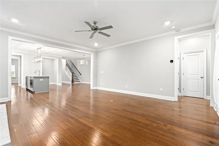 Natural hardwood flooring flows throughout this open-concept living area, leading to a modern kitchen and inviting staircase.
