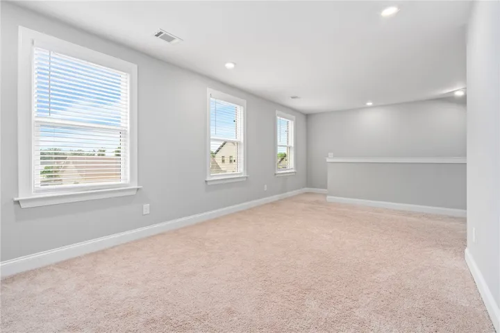 A spacious, naturally illuminated room features plush carpeting and multiple windows.