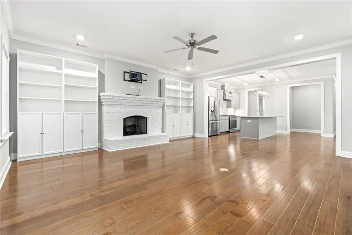 An inviting open-concept living space features warm hardwood floors and a white brick fireplace.