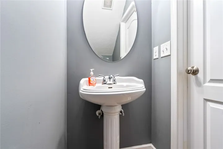 This sleek pedestal sink bathroom features a stylish mirror and a well-maintained door.