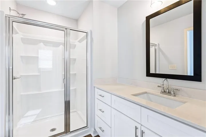 This bright bathroom features a spacious shower and a vanity with a large mirror.
