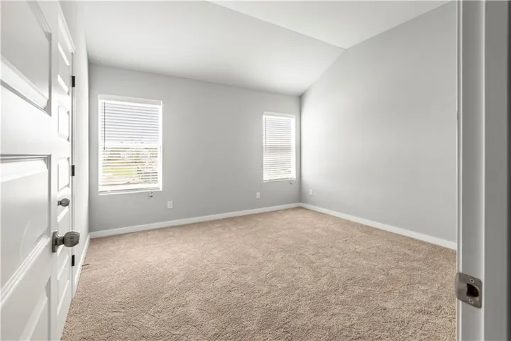 This spacious room features vaulted ceilings, warm carpeting, and natural light from multiple windows.