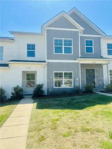 This modern townhome features a crisp exterior and a welcoming pathway set against a bright sky.