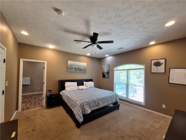 This spacious primary bedroom features soft carpeting, recessed lighting, and a charming arched window.