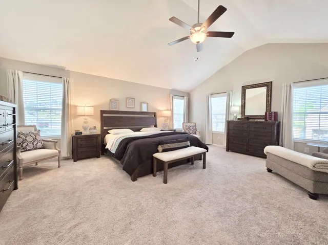 Primary Suite offers high vaulted ceilings, plush carpeting, and ample natural light through multiple windows.