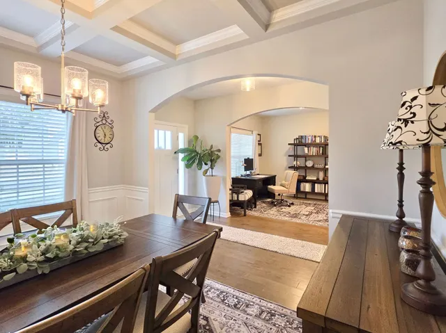 This elegant dining room boasts a coffered ceiling, hardwood floors, and seamless flow into a dedicated home office.