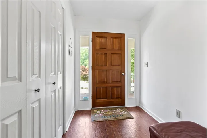 This inviting entryway features rich wood flooring, crisp white walls, and a classic wooden door.