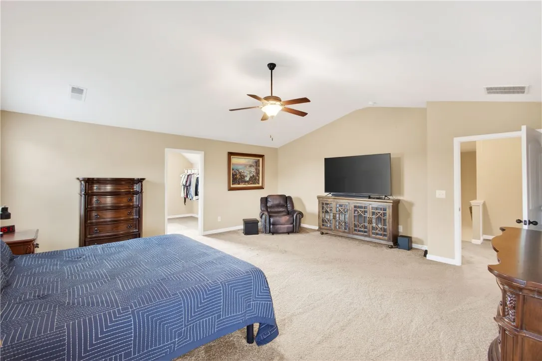This spacious primary bedroom offers plush carpeting and a vaulted ceiling with a fan.