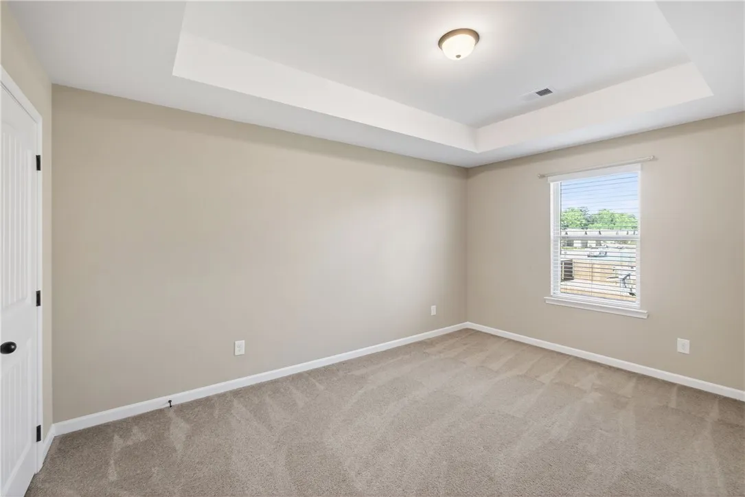 This serene bedroom offers a tranquil retreat with soft carpeting and an elegant tray ceiling.