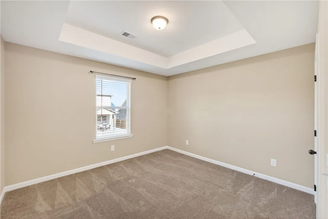 An inviting room features a tray ceiling, soft carpet, and natural light.