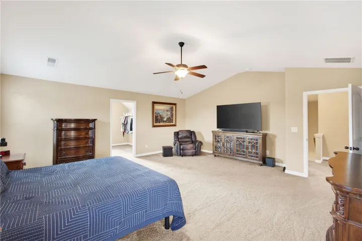 This spacious primary bedroom offers plush carpeting and a vaulted ceiling with a fan.