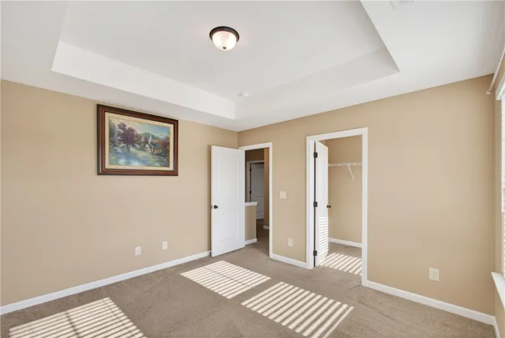 This spacious bedroom features a tray ceiling, plush carpeting, and ample natural light.