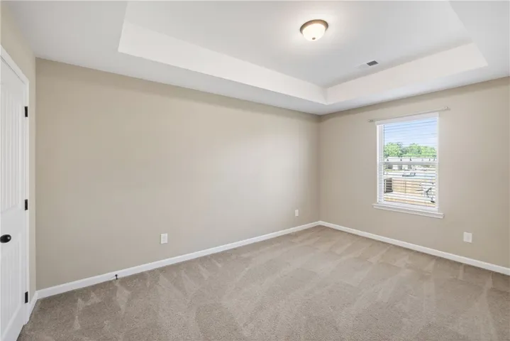 This serene bedroom offers a tranquil retreat with soft carpeting and an elegant tray ceiling.
