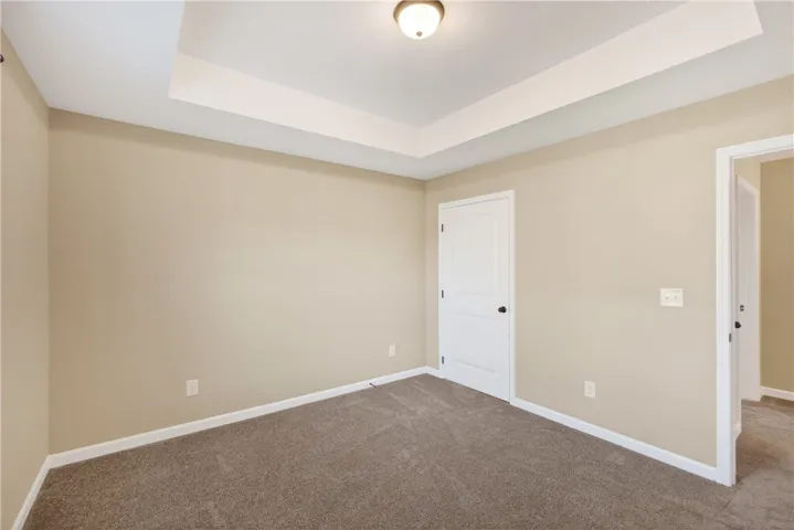 An inviting room features a tray ceiling, plush carpet, and crisp white trim.