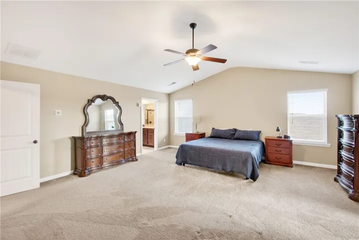 This spacious primary bedroom features soft carpeting, a high vaulted ceiling, and an en-suite bathroom.