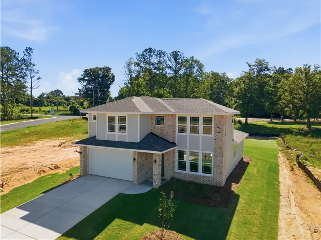 A newly constructed residence features an attached garage and a concrete driveway, blending modern design with a natural setting.