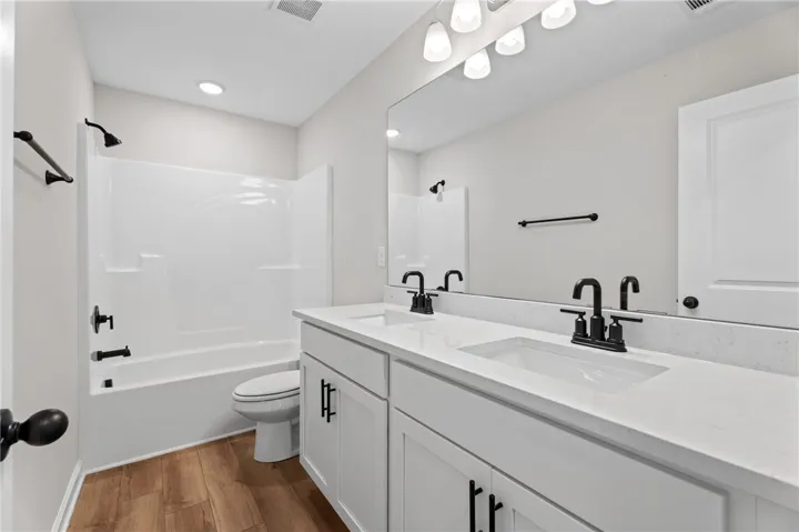 Modern fixtures elevate this pristine bathroom, featuring a double vanity and sleek tub-shower combination.