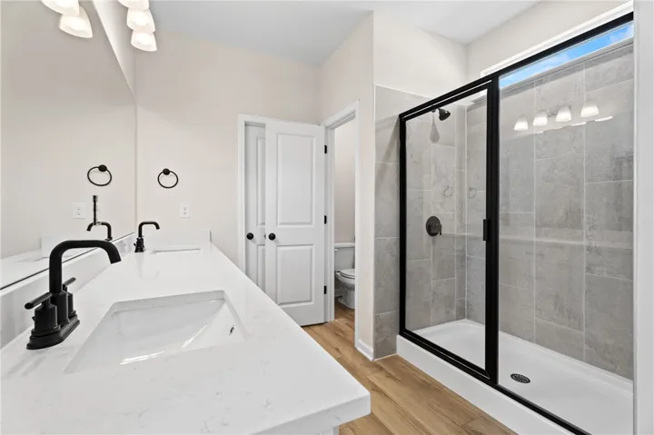 Dual vanity with sleek fixtures offers ample counter space, alongside a modern glass-enclosed shower.