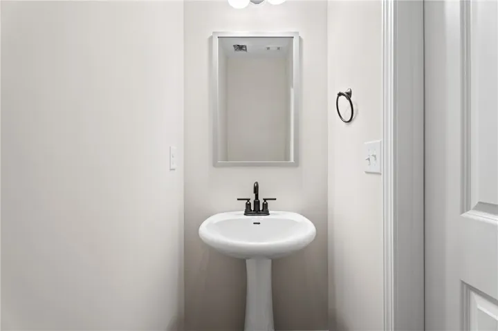A sleek pedestal sink with modern black fixtures anchors this well-appointed powder room.