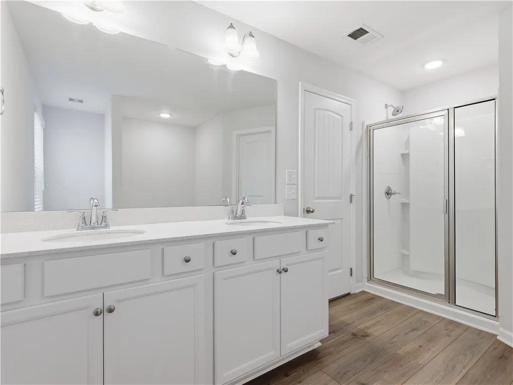 This bright bathroom features a spacious vanity with dual sinks and a sleek glass-enclosed shower.