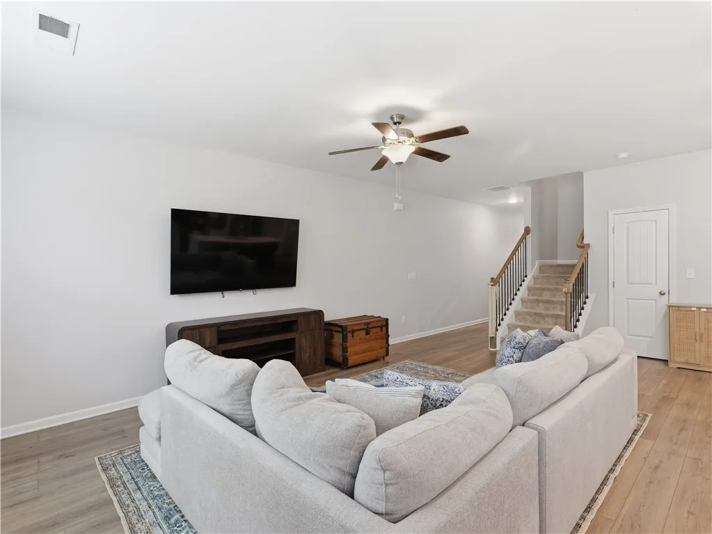 This inviting living space features warm flooring, a functional ceiling fan, and convenient stair access to upper levels.