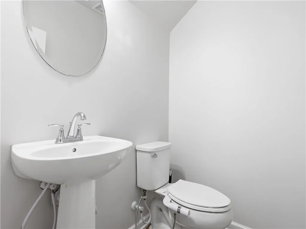 This clean and bright powder room features a classic pedestal sink and toilet, offering convenience.