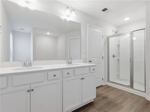 This bright bathroom features a spacious vanity with dual sinks and a sleek glass-enclosed shower.