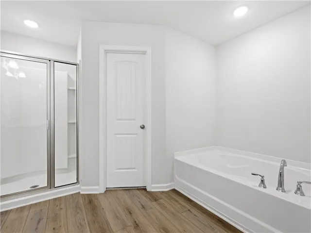 This clean and bright bathroom features a spacious soaking tub and a walk-in shower with clear glass.
