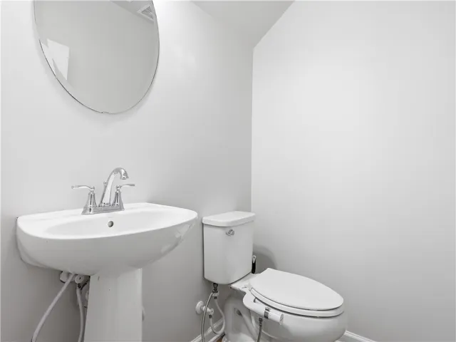 This clean and bright powder room features a classic pedestal sink and toilet, offering convenience.
