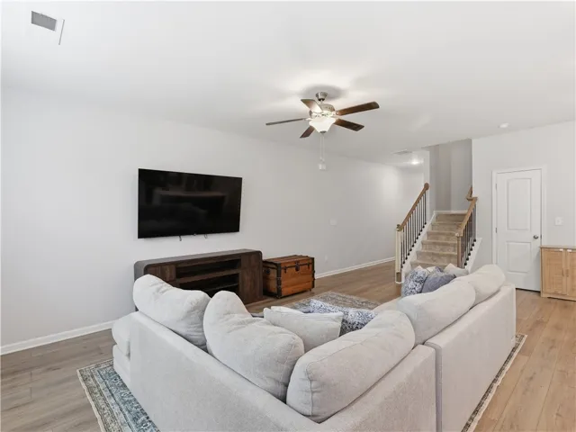 This inviting living space features warm flooring, a functional ceiling fan, and convenient stair access to upper levels.