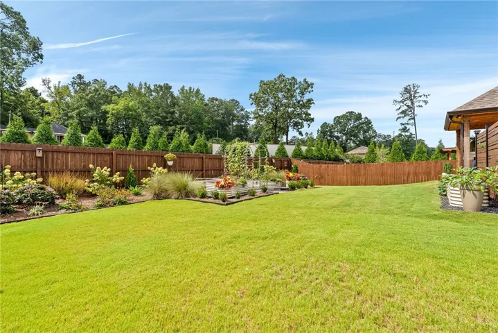 The privacy fence encloses this backyard oasis, featuring raised garden beds, an arbor, carefully chosen plants, and a spacious lawn that create a true vacation-at-home atmosphere.