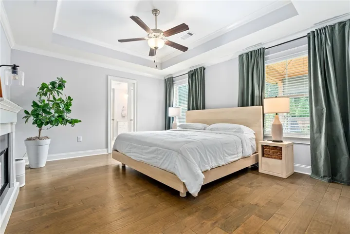 The primary bedroom features the same beautiful wood floors as the common areas, with double windows framing the bed and an electric fireplace adding ambiance.