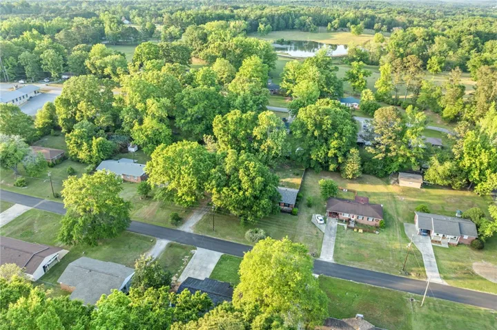 An aerial view showcases a peaceful neighborhood with abundant trees and a tranquil pond nearby.