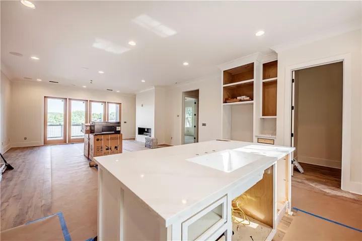 This spacious open-concept room features an expansive kitchen island, built-in shelving, and large windows with serene views.