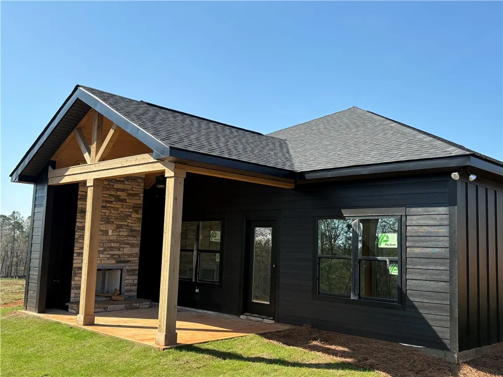This newly constructed home features a stone fireplace, sleek dark siding, and a covered patio.