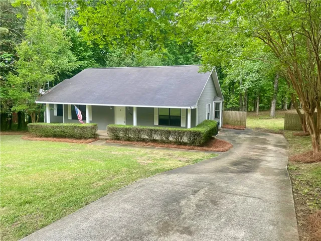This charming home offers a welcoming facade nestled among mature trees and lush greenery.