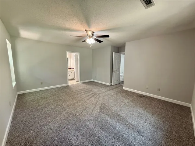 The primary bedroom offers comfortable carpeting and a ceiling fan, leading to a private bathroom.