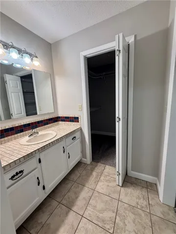This functional bathroom features a single vanity, tiled countertop, and an adjacent walk-in closet for added convenience.