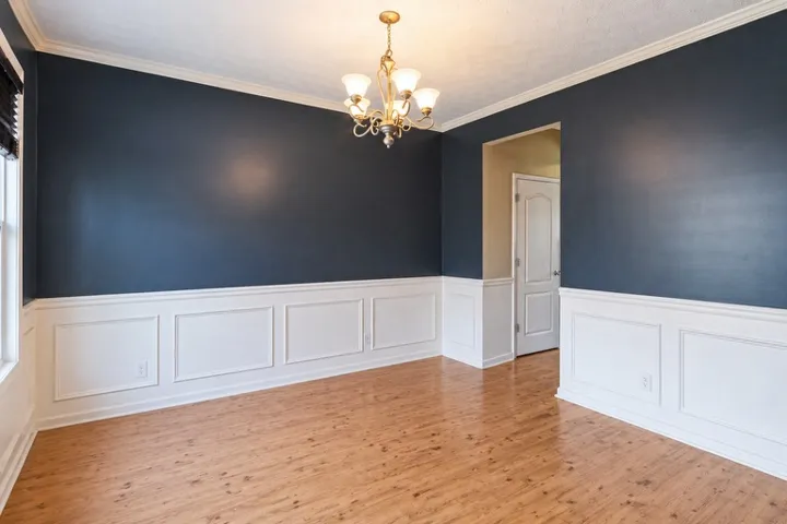 Elegant dining area features wainscoting and a classic chandelier, offering a bright and inviting space.
