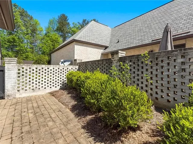 This charming property offers a private yard with a distinctive patterned brick fence and lush landscaping.