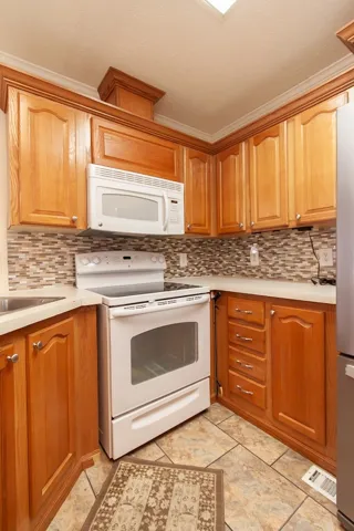 The mobile home kitchen offers warm wooden cabinetry, practical appliances, and durable tile flooring.