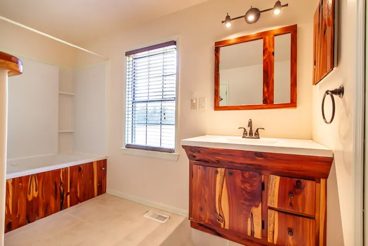 This bathroom features unique wooden cabinetry, a jetted bathtub, and a window for natural light.