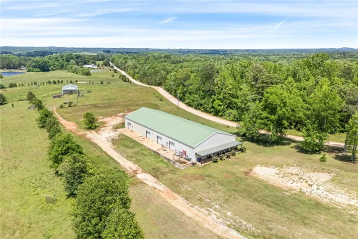 This aerial view showcases a spacious pole barn with a vibrant green roof amidst expansive grounds.
