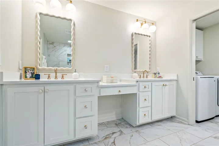 Elegant primary bathroom features dual vanities, bright lighting, and an adjacent laundry area.