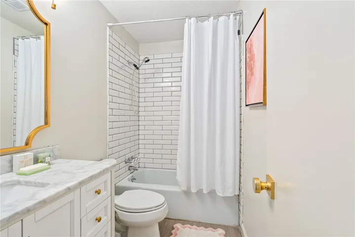 This bright bathroom features subway tile, a shower-tub combination, and a single vanity with a marble countertop.