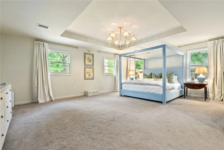 This spacious primary bedroom offers plush carpet flooring, a tray ceiling, and multiple windows.