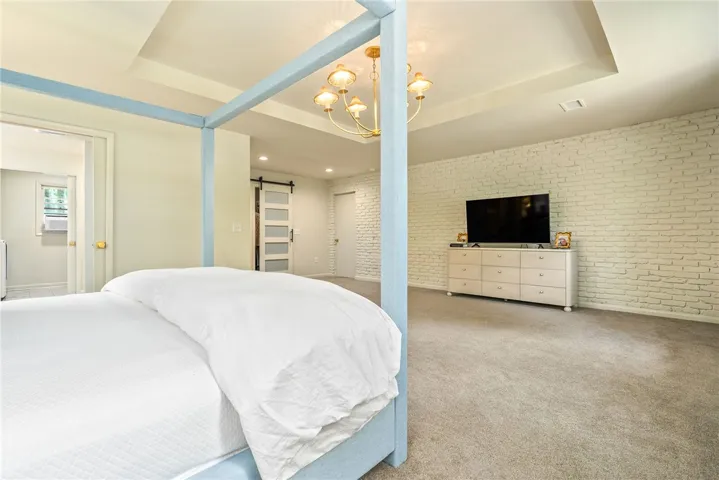 This spacious bedroom offers comfortable carpeting and a distinctive brick accent wall, creating a cozy and inviting atmosphere.