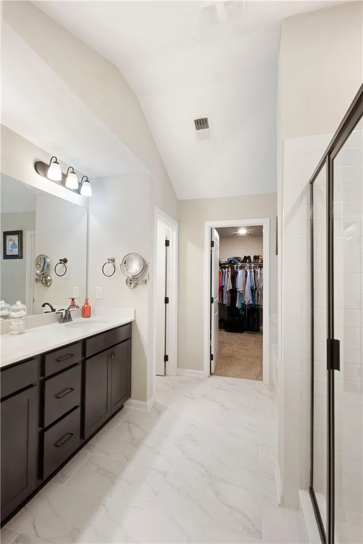 This spacious bathroom offers elegant flooring and a well-appointed vanity with convenient access to a walk-in closet.