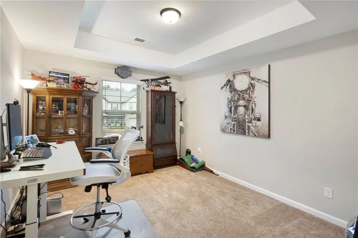 This versatile bedroom features carpet flooring and a tray ceiling, ideal for a home office or creative space.