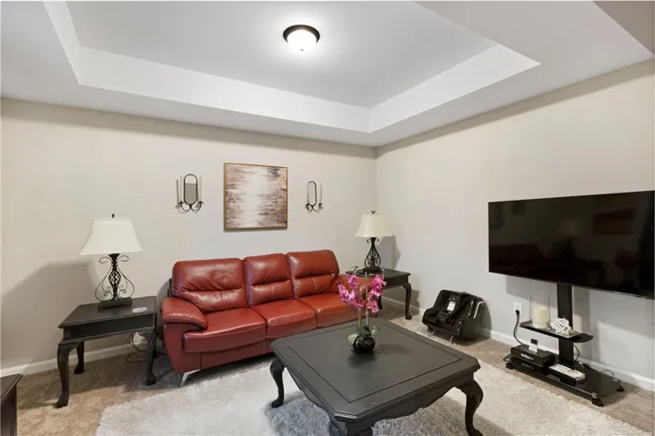 This inviting space in the primary suite features a tray ceiling, soft carpet, and warm natural light.